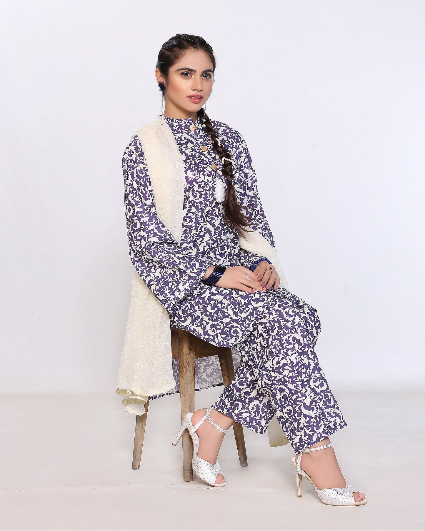 Woman in a floral outfit sitting on a stool against a white background