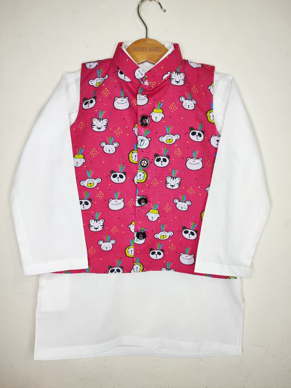 Children's outfit with a white shirt and pink vest featuring cartoon designs on a beige background.